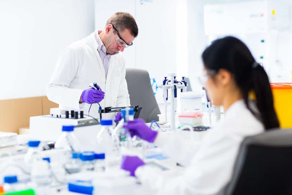 Two scientists wearing lab coats in a lab carrying out experiments